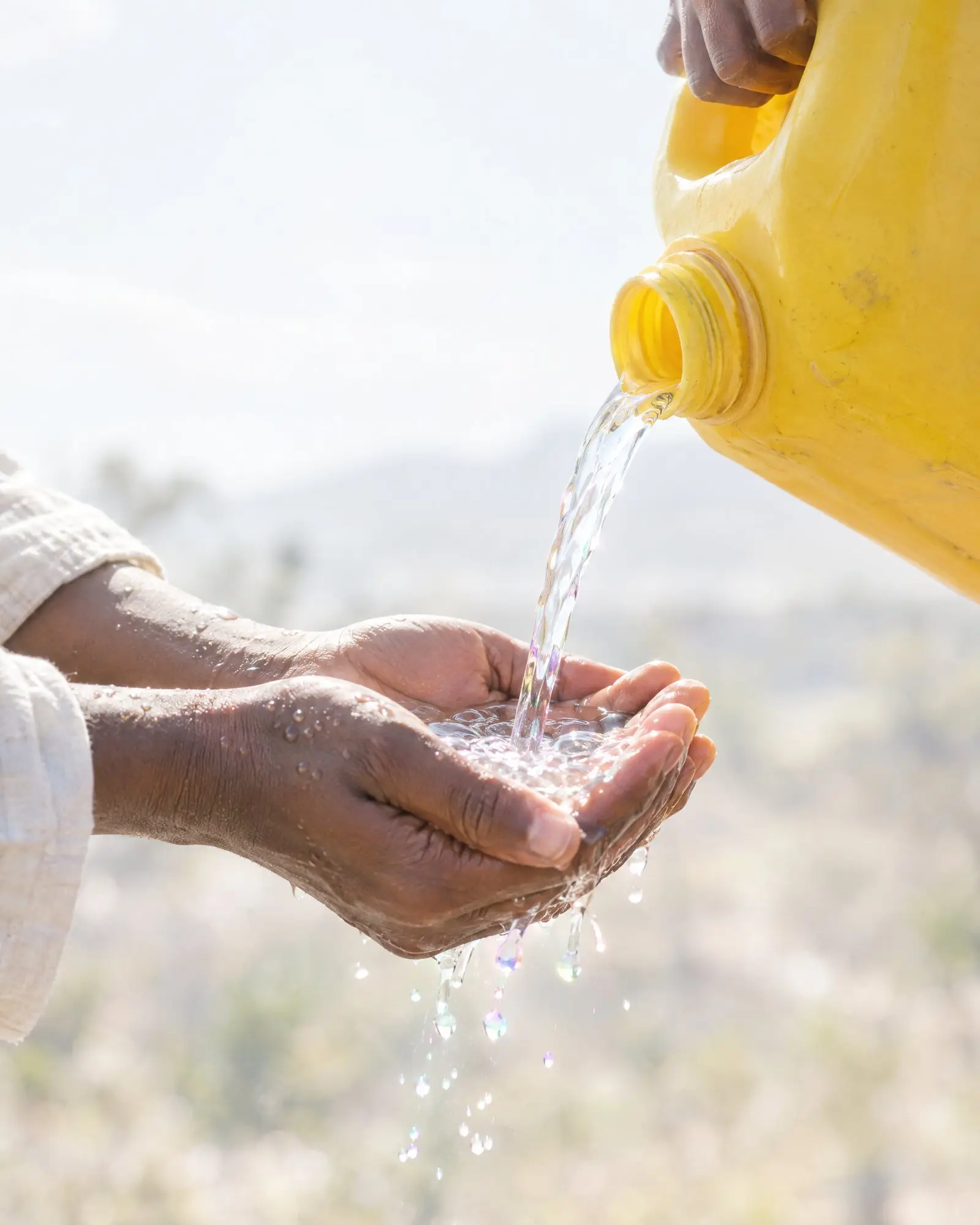 Cupped hands receiving clean water poured from a jerrycan